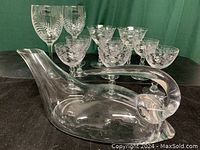 11 pieces of glassware arranged on black surface with green backdrop showing the clear crystal wine duck decanter in front and etched wine glasses behind