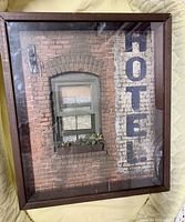 Frontal view of the shadow box sculpture displaying a brick wall with a window and a vertical painted HOTEL sign on the right side.