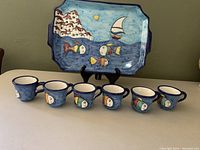 Full set of 6 espresso cups lined up in front of the matching rectangular tray, showing the hand-painted design and size scale.