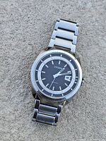 Front angle view of Citizen Eco-Drive watch on textured surface, showing black dial with date and stainless steel bracelet.