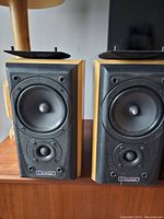 Pair of Mission 771 speakers without grille covers showing the woofers and tweeters on a black surround with wood finish cabinets.