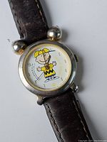 Front view of the vintage Charlie Brown wristwatch with silver-tone round case, cartoon character dial, and brown leather strap showing wear.