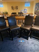 Four dark brown faux leather bar height stools shown side by side in room with blue carpet, illustrating the full set and general condition.