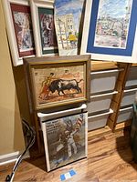Group view of all six artworks leaning against wall next to storage bins
