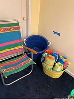 Colorful striped beach chair next to large blue bucket and two plastic carrying buckets on the floor