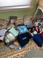 Photo of assorted bed linens on floor, including various packaged and unpackaged items with different colors and patterns.