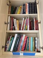 Photo of three shelves of assorted cookbooks and notebooks, various sizes, colors, and bindings visible.
