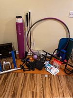 Wide view of exercise equipment including purple foam roller, Pilates reformer, small purple ball, exercise mat, pull up bar, golf clubs, and other fitness accessories on wooden floor