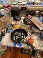 Photo showing Calphalon integrated skillets, bamboo skewers, coffee maker, glass pitcher, and assorted kitchen utensils and tools spread on a white cloth on a table.