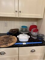 Overview photo showing all items including Pyrex and Rubbermaid storage containers, pizza stone, and Corningware covered casserole dish arranged on countertop.