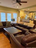 Overview of brown leather sofa, loveseat, club chair and wood tables in living room.