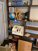 Shelving unit containing multiple items including lockboxes, globe puzzle, desk organizers, lamp, books, corkboard, and decorative pieces.
