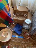 Lot arranged on carpet including margarita glasses, napkins, salt rimmer, beverage dispenser with stand, chip and dip bowl, folded festive tablecloth.