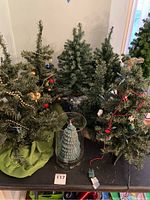 Four mini artificial Christmas trees and one Christmas tree candle arranged on a table, showing overall lot contents including decorations and holders.