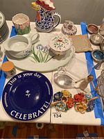 Various painted serving pieces and decorative items displayed including plates, pitchers, candlestick holders, and figurines.