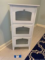 Full front view of cabinet with three closed drop-down doors with beveled glass panels and silver oval knobs.