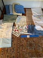Photo showing the folded assorted linens including placemats, napkins, tablecloths, and runners arranged on the floor against a white wall.