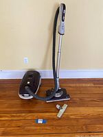 Kenmore vacuum cleaner with hose, floor attachment, and separate rug attachment on hardwood floor against beige wall.
