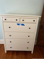 Front view of the white dresser showing 6 drawers with black metal knobs.