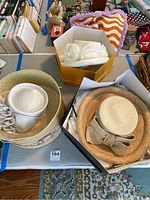 Set of three beige straw hats with decorative bows and flowers displayed inside and beside matching hat boxes on a table.