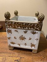 Front view of the porcelain planter showing gold painted floral decorations and decorative finials on each corner