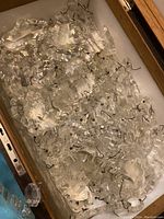 Collection of clear faceted crystal chandelier pieces with metal hooks inside a drawer or box