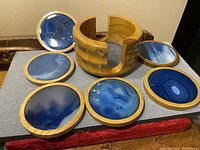Six deep blue agate stone coasters with light wood frames arranged around their matching wooden holder on a tray.