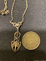 Close-up photo of the antique Edwardian gold necklace pendant next to a coin for size reference, shows detailed marcasite stone arrangement and pendant design.