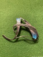 Close-up image of the brooch on green background showing the curved Art Deco design and blue enamel accents.