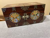 Closed view of the Asian double cube jewelry box showing the wood finish, brass corner plates, and round mother of pearl inlay on front doors with latch.