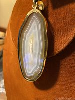 Close-up image of the brown agate slice pendant with gold-tone metal edging showing the natural banding pattern in the stone.