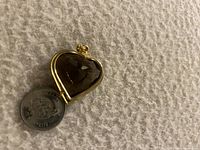 Heart shaped purple stone pendant next to a quarter for size comparison, showing gold-tone metal setting
