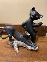 Front view showing black ceramic cat vase with arm raised and black panther stretching on a log base in front