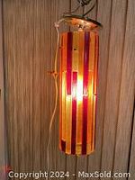 Full frontal shot of the hanging lucite lamp showing vertical red, yellow, and orange panels with satin brass canopy.