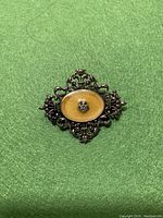 Front view of Victorian style sterling silver brooch on green background highlighting the central yellow/gold enamel oval with flower detail and ornate silver filigree design.
