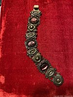 Full view of vintage brass bracelet with purple stones on red fabric background.