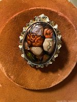 Front view of the vintage enameled pendant/brooch showing the detailed painted profile of a woman with red hair in an ornate metal setting, placed on a round reddish-brown velvet surface.
