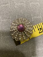 Top view of the round vintage silver filigree brooch with a central amethyst stone, shown alongside measuring tape indicating size.