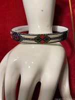 Close-up side view of the white enameled cuff bangle showing colorful folk design motifs in red, green, and blue colors with black and white borders.
