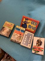 Five vintage card game decks including Authors, Home-Run Baseball, Old Maid, Touchdown Football, and a standard deck on a blue surface.