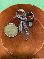 Front view of the vintage sterling silver ribbon bow brooch with marcasite stones next to a coin for size reference.