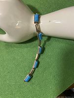 Bracelet displayed on a white mannequin hand, showing the turquoise stones and chain links from top view.