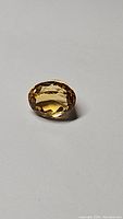 Oval cut golden citrine gemstone photographed on a grey background showing facets and color.