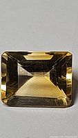 Close-up photo of the rectangular emerald cut golden citrine gemstone showing its facets and color.