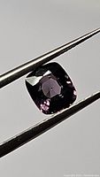 Front angled view of the cushion cut deep purple spinel gemstone held by tweezers.