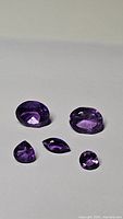 Five natural Brazilian amethyst gemstones of various cuts and sizes laid out on a white surface.