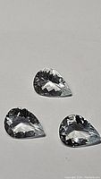 Three pear-shaped clear off white aquamarine gemstones placed on a white background, showing their color, cut and clarity.