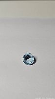 Round cut sky blue topaz gemstone placed on a light surface, showing its size and clarity.