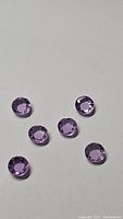 Six faceted round amethyst gemstones arranged on white background showing their pink purple coloration and sparkling facets.
