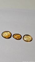 Three natural golden citrine stones laid out on a white background showing various sizes and shades of golden yellow.